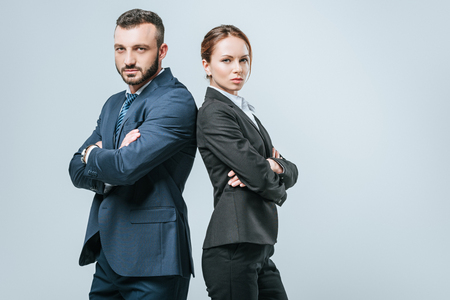 businesswoman and businessman standing with crossed arms and looking at camera isolated on greyの写真素材