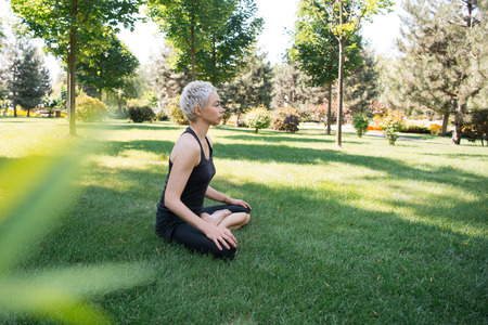 side view of woman practicing yoga in lotus pose on grass in parkの写真素材
