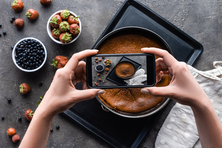 cropped shot of woman taking picture of homemade pie on dark grey tabletopの写真素材