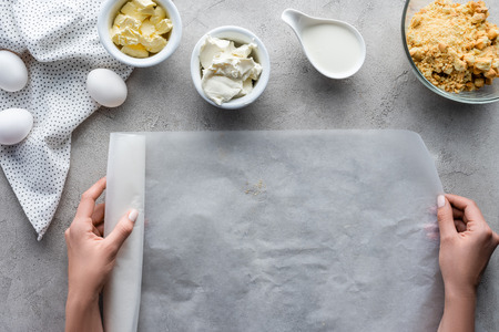 cropped shot of woman holding baking paper with arranged ingredients for pie on grey tabletopの写真素材