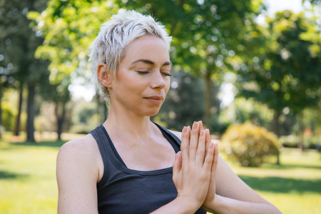 woman practicing yoga with closed eyes and making namaste gesture with hands in parkの写真素材