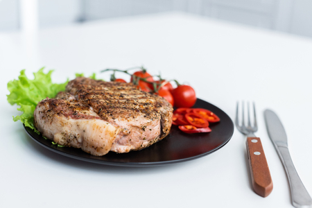 close-up view of delicious grilled steak with lettuce, pepper and cherry tomatoes on black plateの写真素材