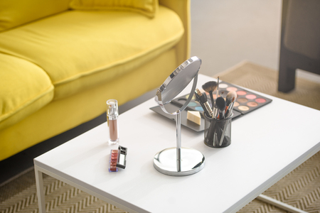 close up view of yellow sofa, mirror, makeup brushes and cosmetics on coffee tableの写真素材