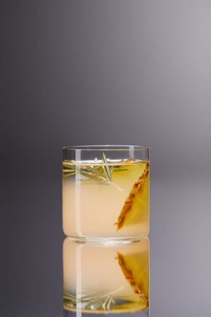 glass of fresh pineapple cocktail on reflective surface and on greyの写真素材