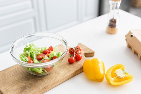 high angle view of glass bowl and fresh vegetables on wooden cutting boardの写真素材