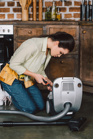 attractive young repairwoman fixing vacuum cleaner with screwdriverの写真素材