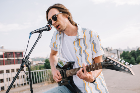 Young man in sunglasses playing guitar and singing in urban environment