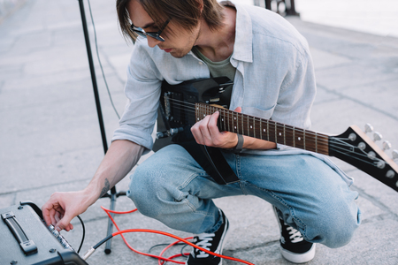 Young man adjusting guitar amplifier while performing on streetの写真素材