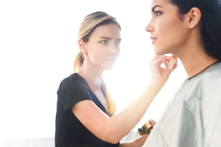 selective focus of beautiful young woman getting makeup done by focused makeup artistの写真素材