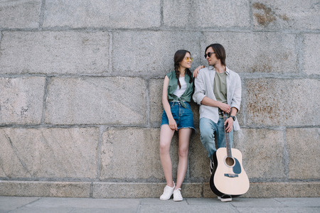 Attractive girl and man with guitar with guitar looking at each other on sunny city streetの写真素材