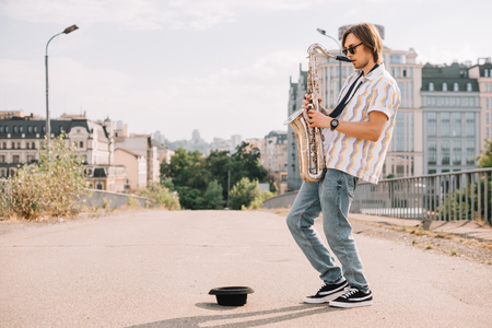 Young happy male busker playing saxophone at city streetの写真素材