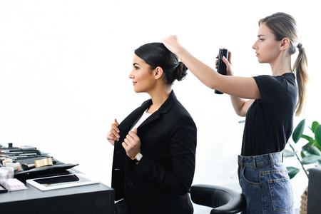side view of businesswoman getting hairstyle fixated with hair spray by hairstylistの写真素材