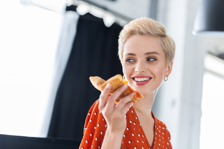 close up portrait of smiling woman holding slice of pizzaの写真素材