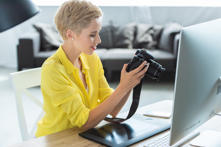 side view of female photographer looking at camera screen at table with graphic tablet and computerの写真素材