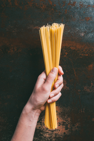 cropped image of man holding raw spaghetti over rustic metal tabletopの写真素材