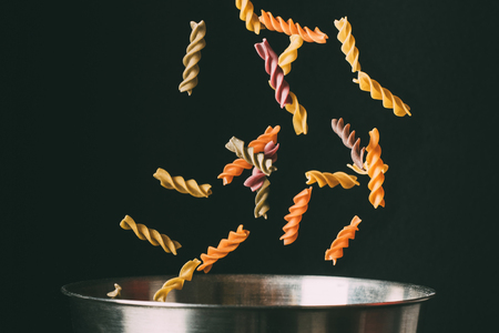 close up shot of colorful fusilli falling into pan on black backgroundの写真素材