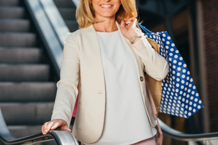 cropped image of smiling woman standing on escalator with shopping bags in mallの写真素材