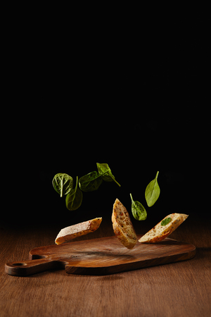 Bread pieces and salad leaves flying above wooden cutting boardの写真素材