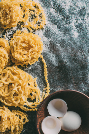 elevated view of raw pasta, bowl with egg and egg shell on table covered by flourの写真素材