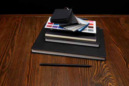 close up view of black notebooks, colors pallet and pencil on wooden tabletopの写真素材