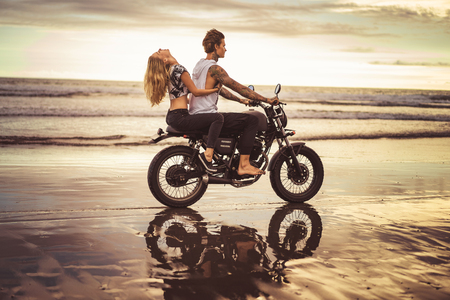 side view of girlfriend hugging boyfriend from back on motorcycle on ocean beachの写真素材