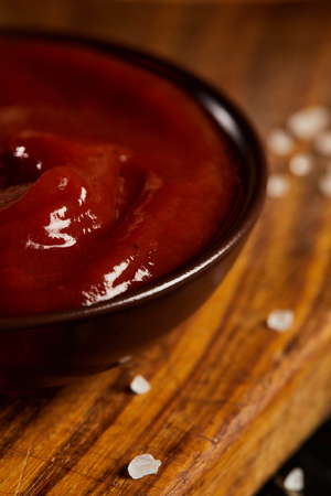 Ketchup in served saucer on wooden board with salt