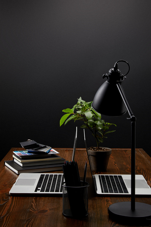 close up view of designer workplace with laptops, notebooks and pallet on wooden tabletop on black wall backdropの写真素材