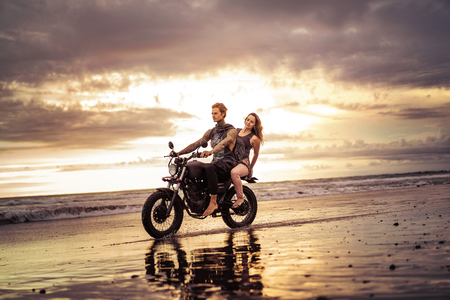 couple riding motorcycle on ocean beach with beautiful sunrise on backgroundの写真素材