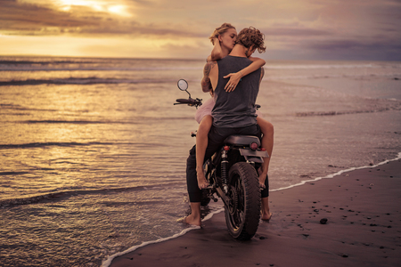 couple hugging on motorcycle on ocean beach during beautiful sunriseの写真素材