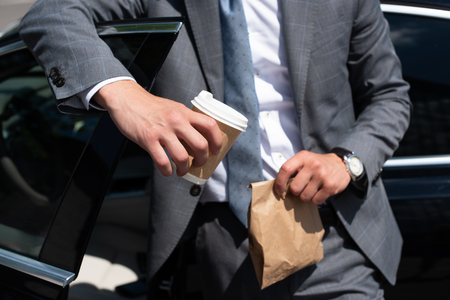 partial view of businessman with take away food and coffee to go standing at carの写真素材