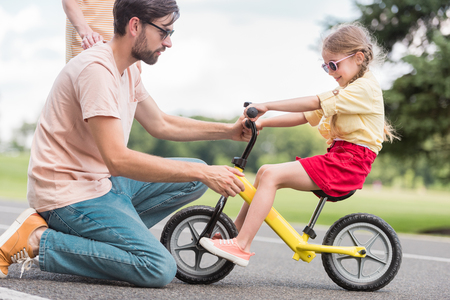 side view of young father teaching little daughter riding bicycle in parkの写真素材