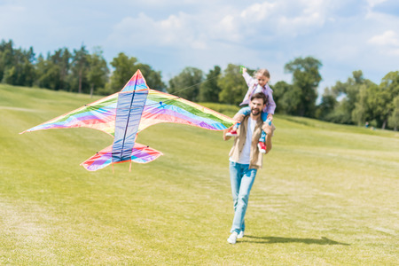 happy father and cute little daughter playing with colorful kite in parkの写真素材