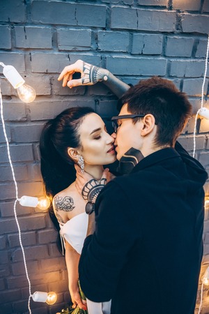 young bride and groom embracing and kissing under grey brick wallの写真素材