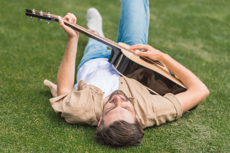 young man lying on grass and playing acoustic guitarの写真素材