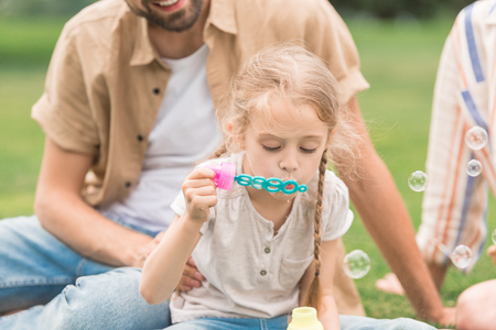cropped shot of parents looking at cute little daughter blowing soap bubbles in parkの写真素材