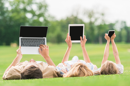 family lying on grass and using digital devices with blank screensの写真素材