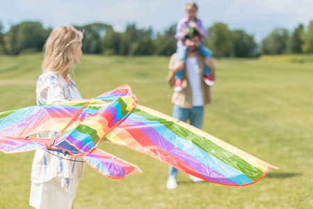 young woman holding  kite while father carrying little daughter on neck behind in park