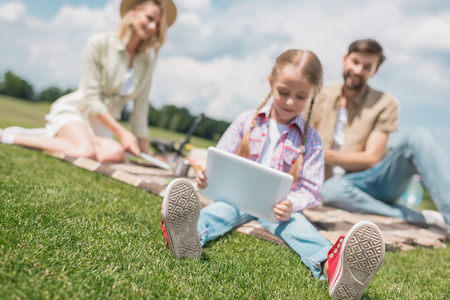child using digital tablet while parents sitting behind at picnicの写真素材