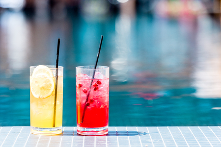close-up shot of glasses of delicious red and orange cocktails on poolsideの写真素材