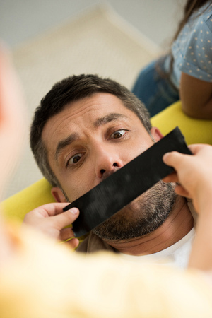 high angle view of children closing father mouth with black tape at homeの写真素材