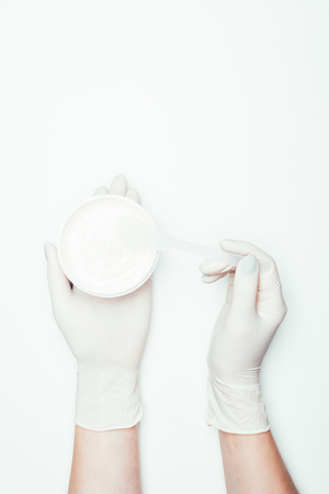 cropped image of woman in latex gloves holding container with clay mask and spoon isolated on whiteの写真素材