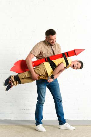 father holding son with toy rocket on back at homeの写真素材
