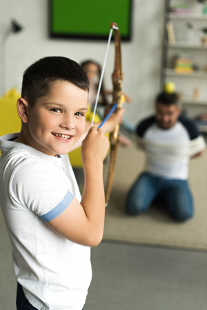son playing with tied father and pretending shooting with toy bow at home