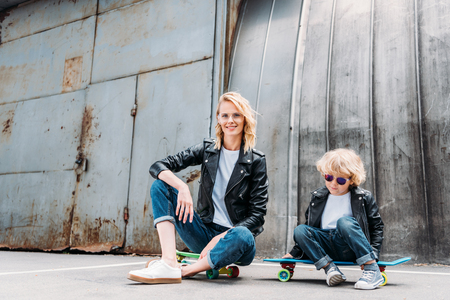 mother and son sitting on skateboards on streetの写真素材