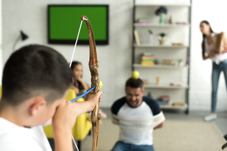 son playing with tied father and pretending shooting with toy bow at homeの写真素材