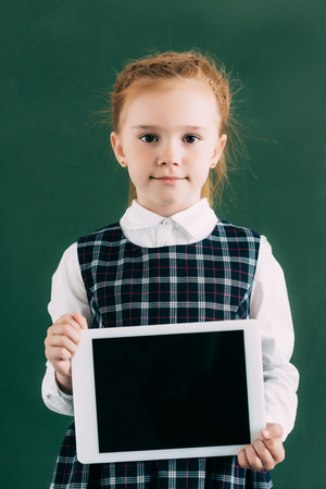 beautiful little schoolgirl holding digital tablet with blank screen and looking at cameraの写真素材