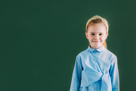 adorable little redhead schoolgirl standing near blackboard and smiling at cameraの写真素材
