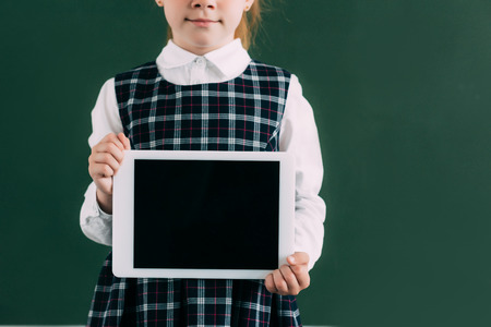 cropped shot of cute little schoolgirl holding digital tablet with blank screen