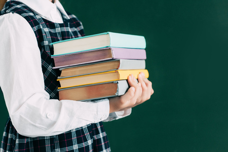 cropped shot of schoolgirl holding pile of books while standing near blackboardの写真素材