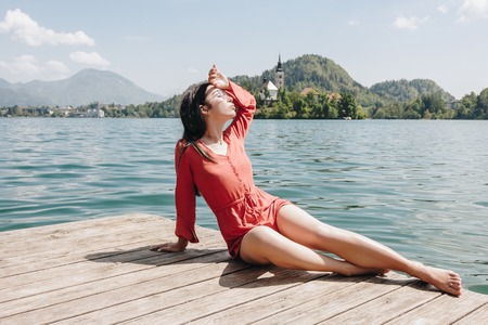 beautiful young woman resting on wooden pier at scenic mountain lake, bled, sloveniaの写真素材